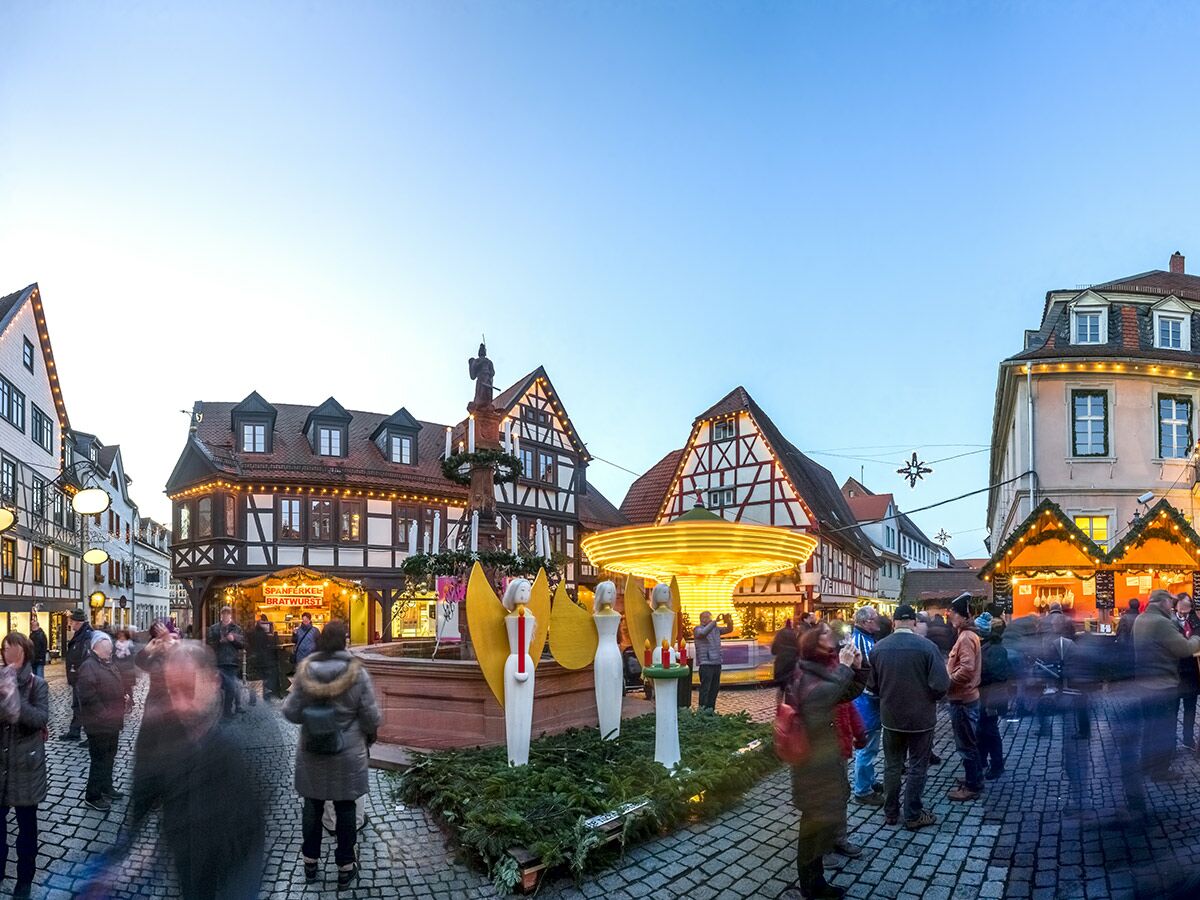 Festlicher Weihnachtsmarkt in einer historischen deutschen Stadt mit beleuchteten Fachwerkhäusern, Karussell, Verkaufsständen und Besuchern.