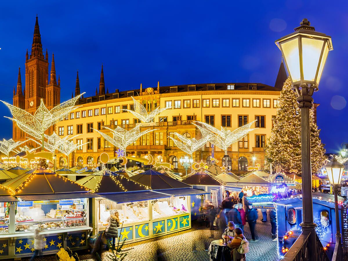 Festlicher Weihnachtsmarkt in Wiesbaden bei Nacht mit Ständen, Lichtern, großem Baum und Marktkirche im Hintergrund.