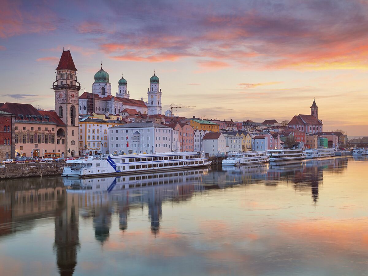 Malerisches Passau bei Sonnenuntergang: Dom St. Stephan, Altes Rathaus, bunte Häuser und Flussschiffe an der Donau mit Reflexionen.