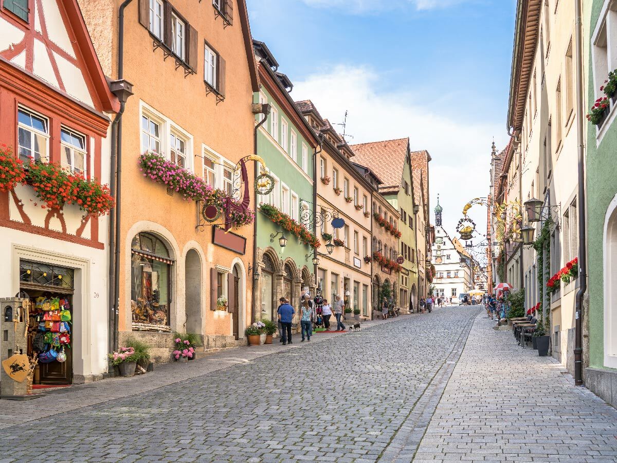 Historische Gasse mit bunten Fachwerkhäusern, Kopfsteinpflaster und Blumenkästen in Rothenburg ob der Tauber bei Tag.