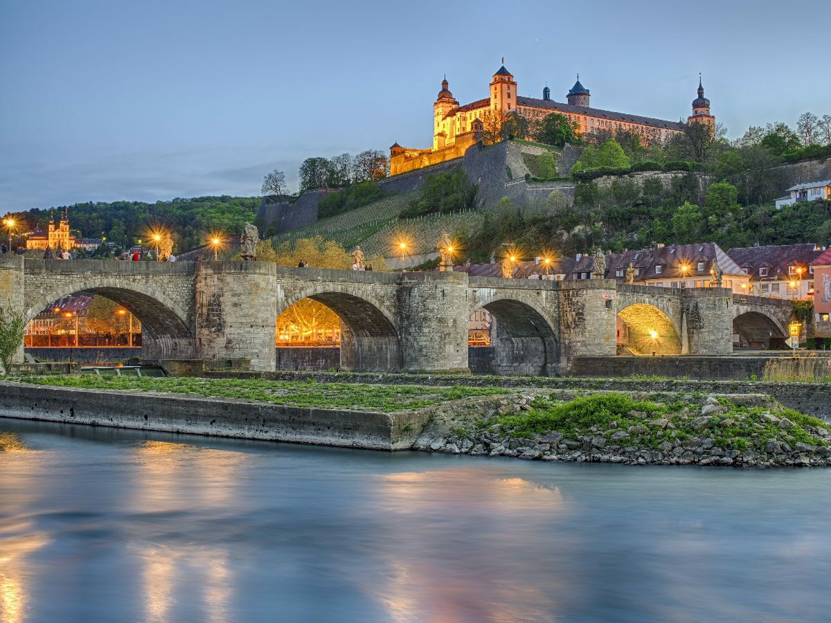 Die beleuchtete Alte Mainbrücke in Würzburg bei Sonnenuntergang mit der Festung Marienberg und dem Fluss Main.