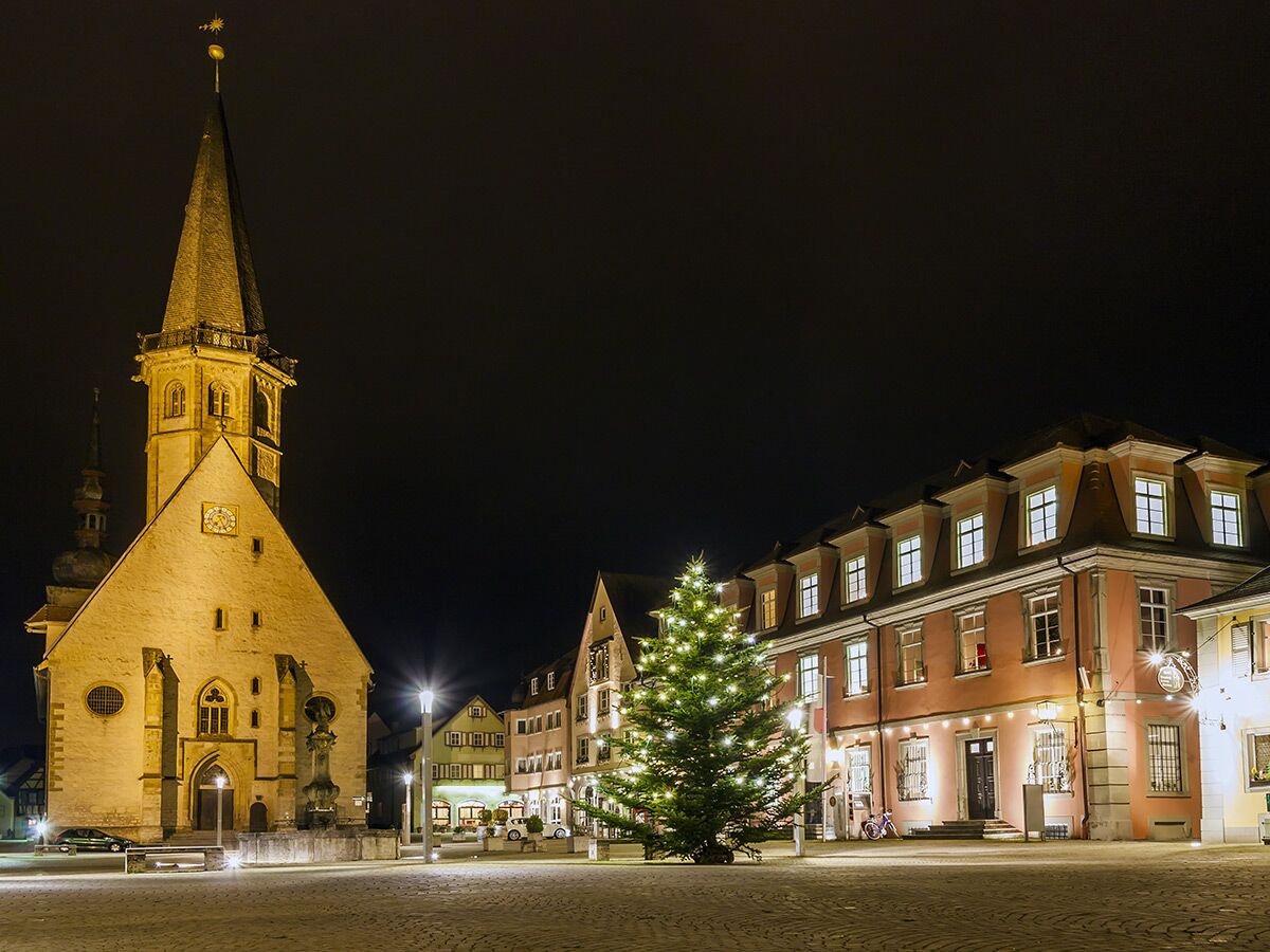 Historischer deutscher Stadtplatz bei Nacht mit beleuchteter Kirche, Weihnachtsbaum und charmanten Altstadtgebäuden.