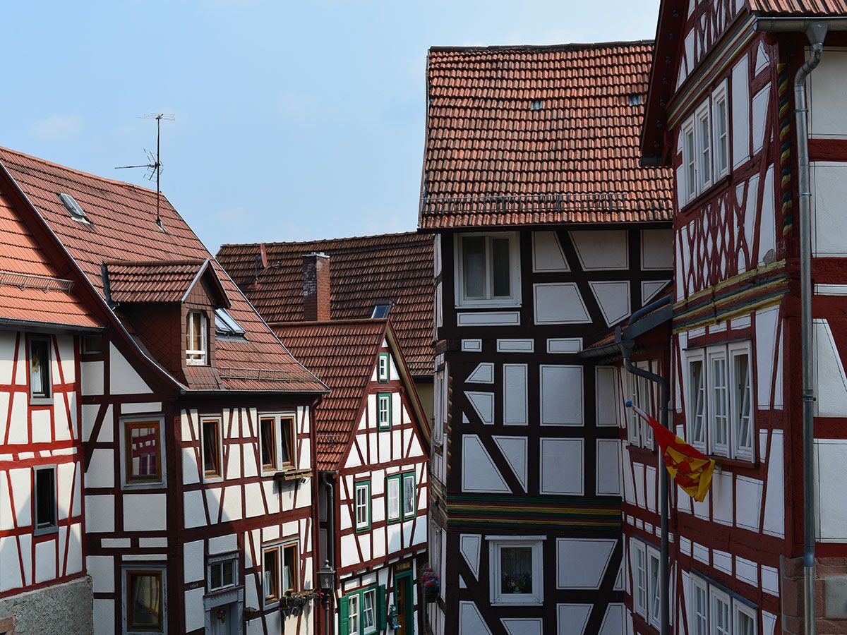 Mehrere historische Fachwerkhäuser mit roten Ziegeldächern und markanten Holzbalken unter blauem Himmel in Deutschland.