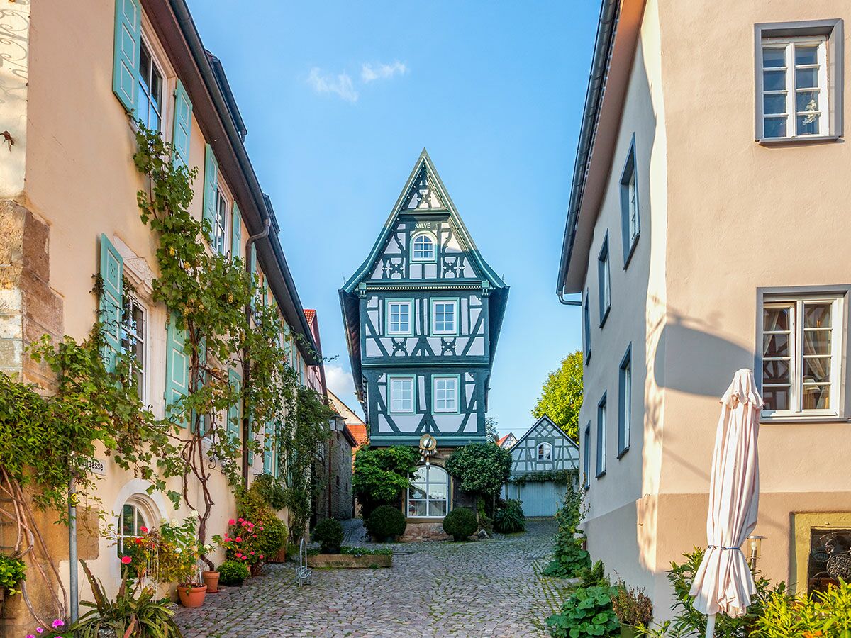 Malerisches Fachwerkhaus am Ende einer historischen Kopfsteinpflastergasse, umgeben von Gebäuden mit Fensterläden und Pflanzen.