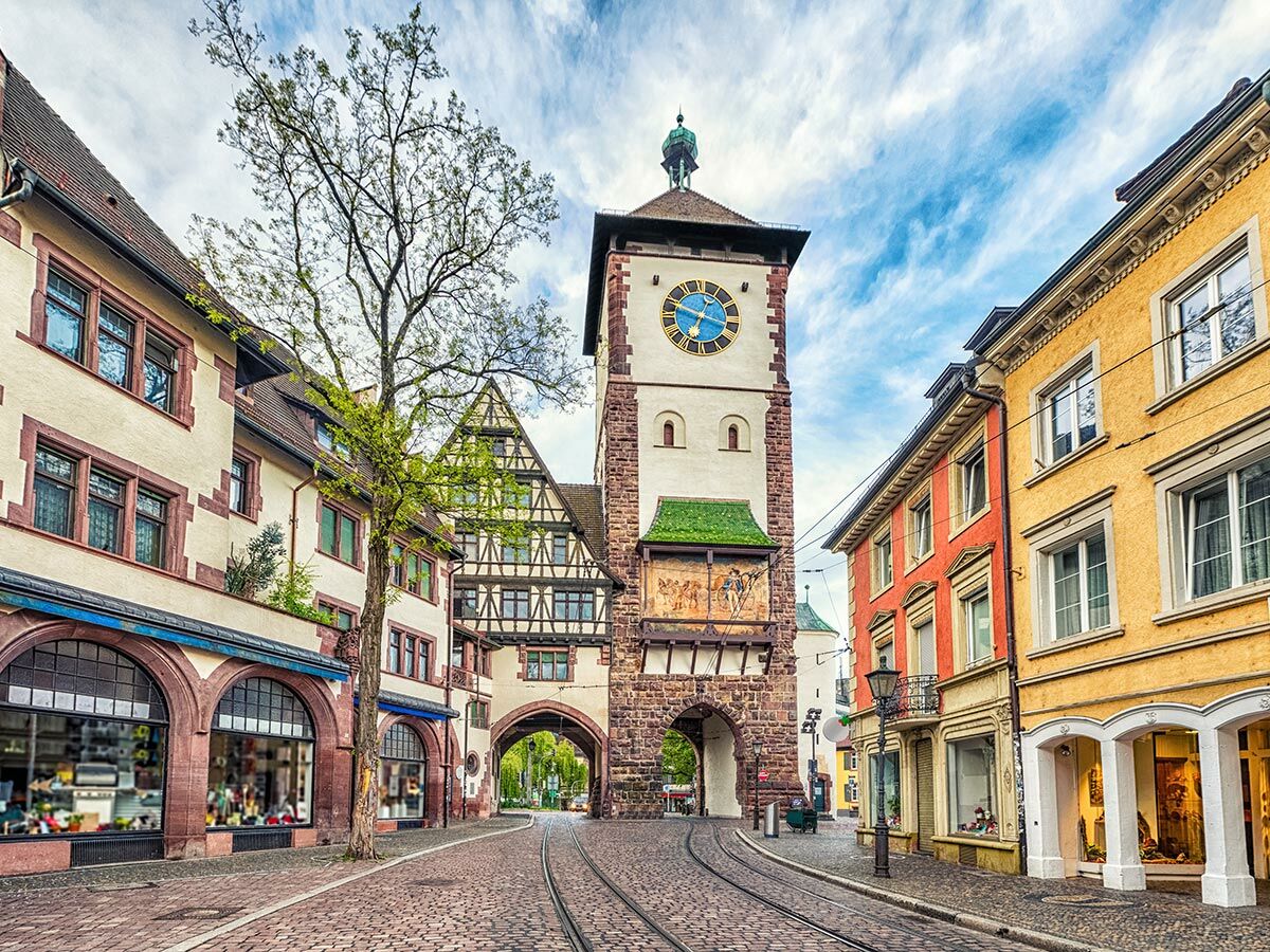 Martinstor in Freiburg im Breisgau mit Glockenturm, Torbogen, Kopfsteinpflasterstraße und historischen Gebäuden bei Sonnenschein.