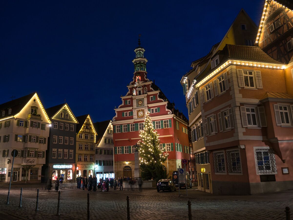 Historisches Ulmer Rathaus und festlich beleuchteter Marktplatz bei Nacht mit Weihnachtsbaum und Menschen.