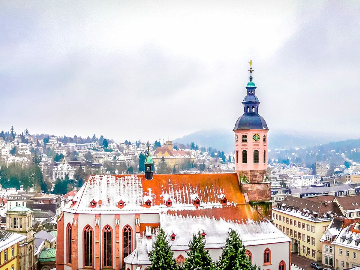 Historische Stiftskirche Baden-Baden mit rosafarbenem Turm und schneebedeckten Dächern in deutscher Winterlandschaft.