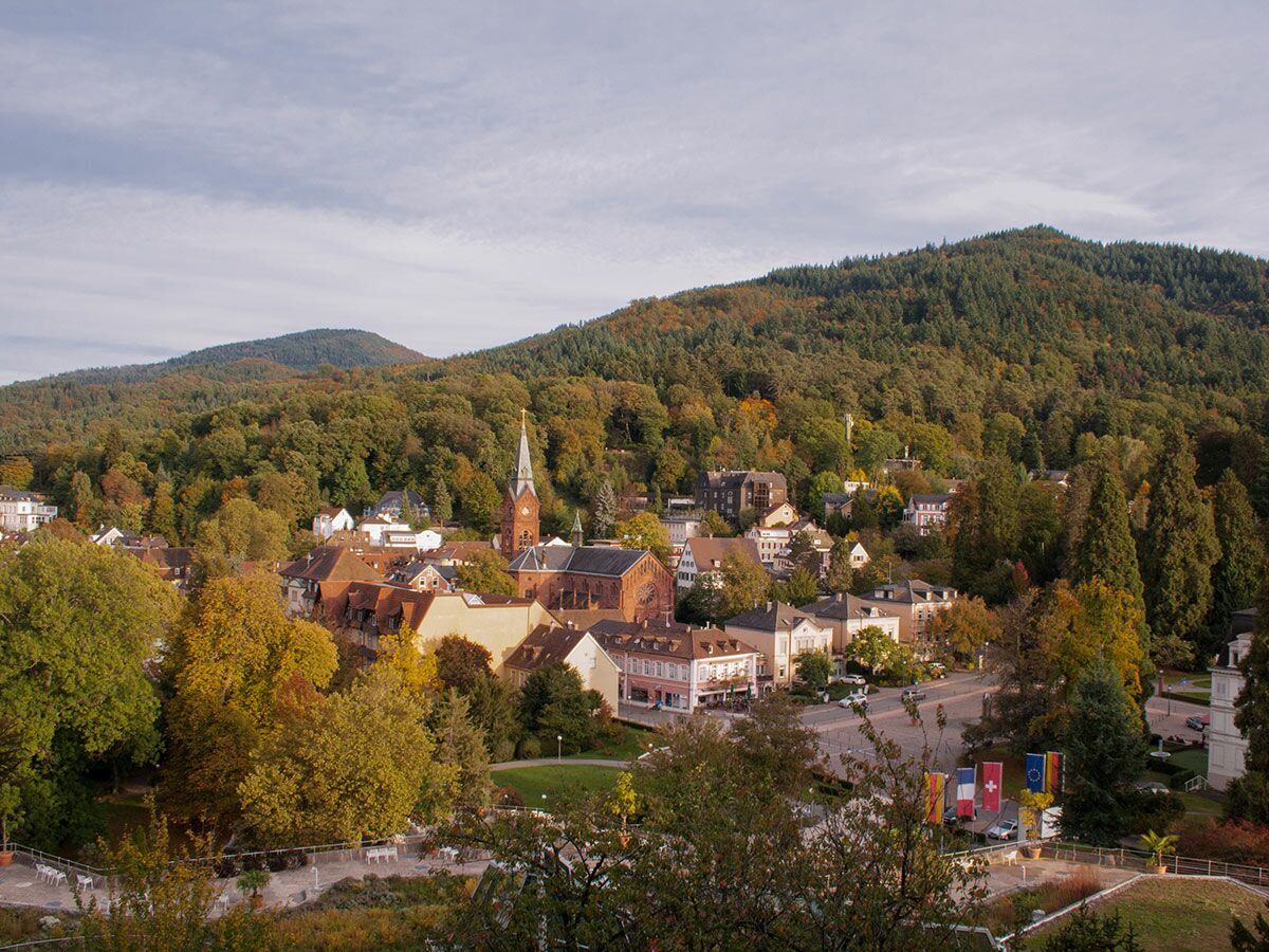 Malerische europäische Stadt im Herbst mit markanter Kirche, traditionellen Gebäuden und bunten Wäldern in hügeliger Landschaft.