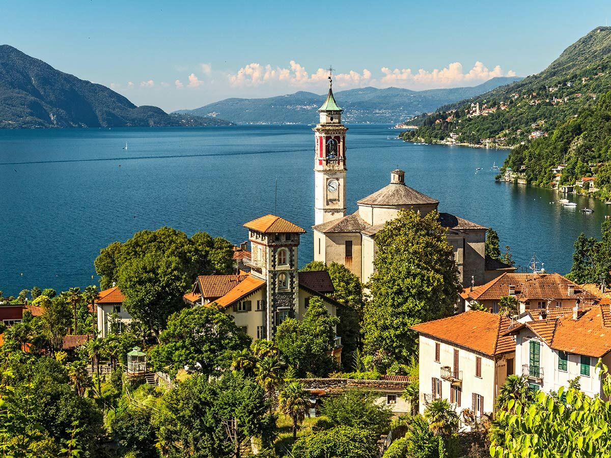 Panoramablick auf Orselina mit Wallfahrtskirche Madonna del Sasso am Lago Maggiore, umgeben von Bergen und üppiger Vegetation.