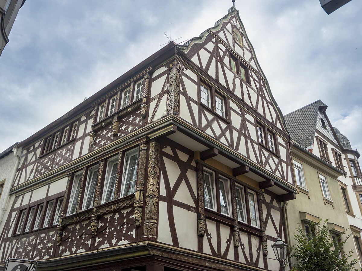 Ornate historisches Fachwerkhaus mit Holzbalken, weißen Wänden und geschnitzten Verzierungen unter bewölktem Himmel.