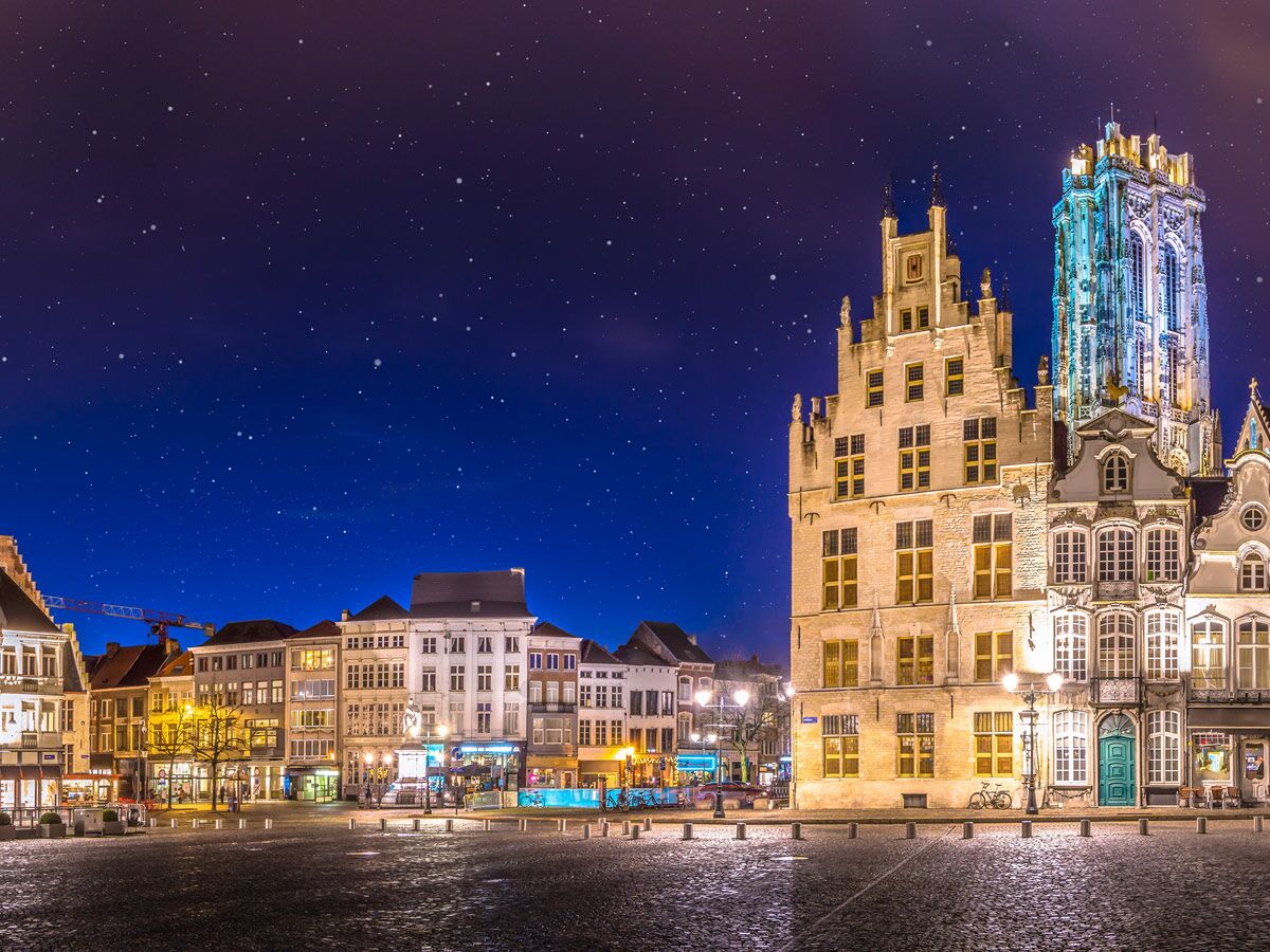 Nächtlicher Grote Markt in Mechelen, Belgien, mit historischen beleuchteten Gebäuden, einem Belfried und Sternenhimmel.