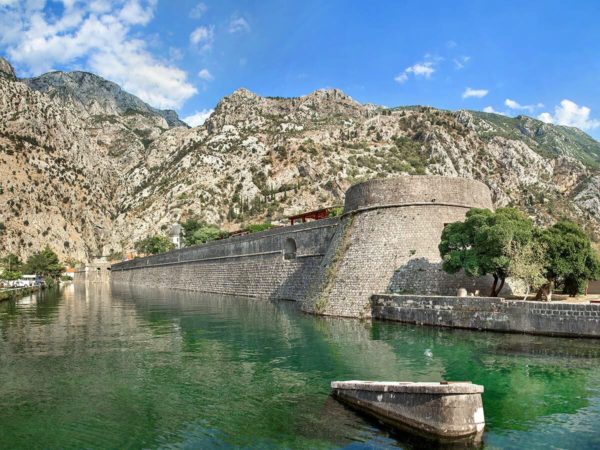 Historische Stadtmauer und Bastion von Kotor, Montenegro, am smaragdgrünen Wasser mit imposanten Bergen im Hintergrund.