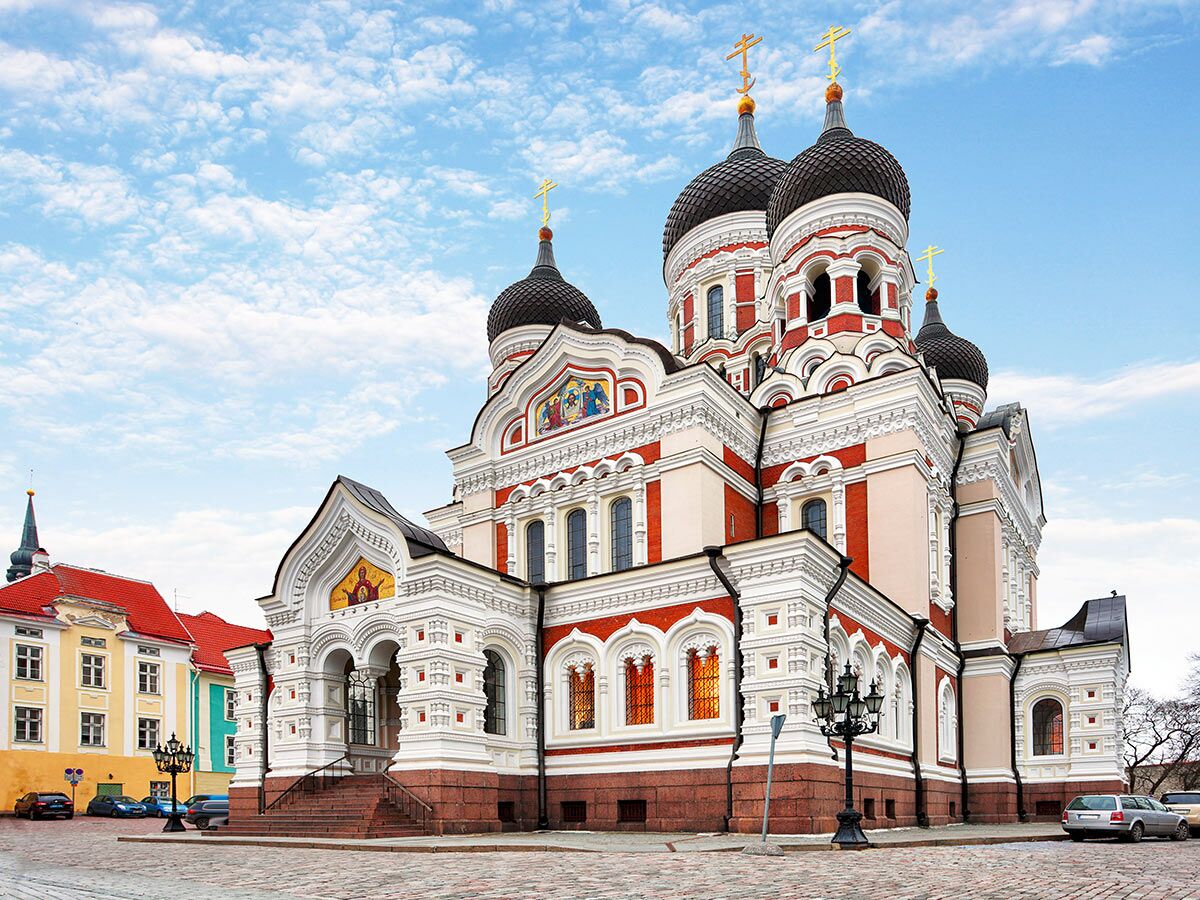 Die Alexander-Newski-Kathedrale in Tallinn, Estland, mit Zwiebelkuppeln, goldenen Kreuzen und roter-weißer Fassade unter blauem Himmel.