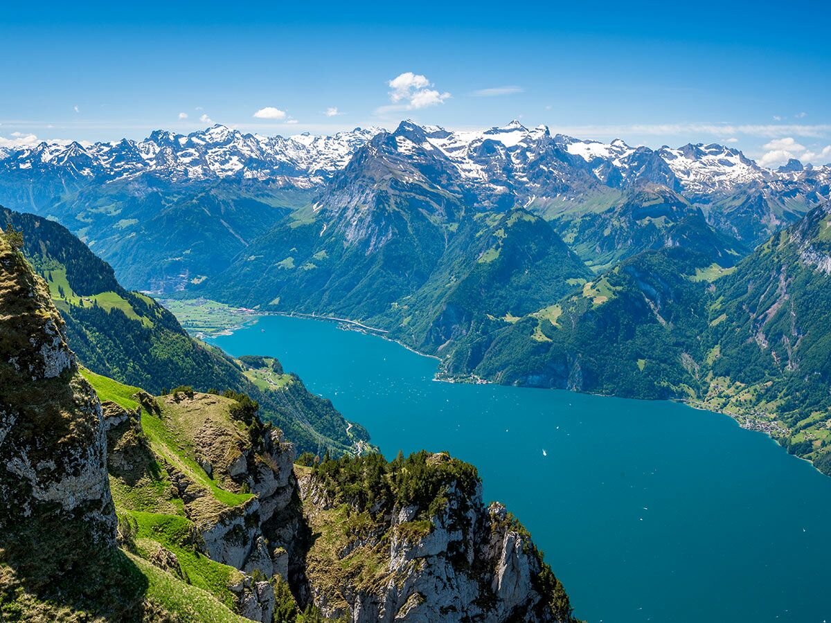 Atemberaubender Blick auf einen türkisblauen See inmitten schneebedeckter Schweizer Alpen und grüner Täler.