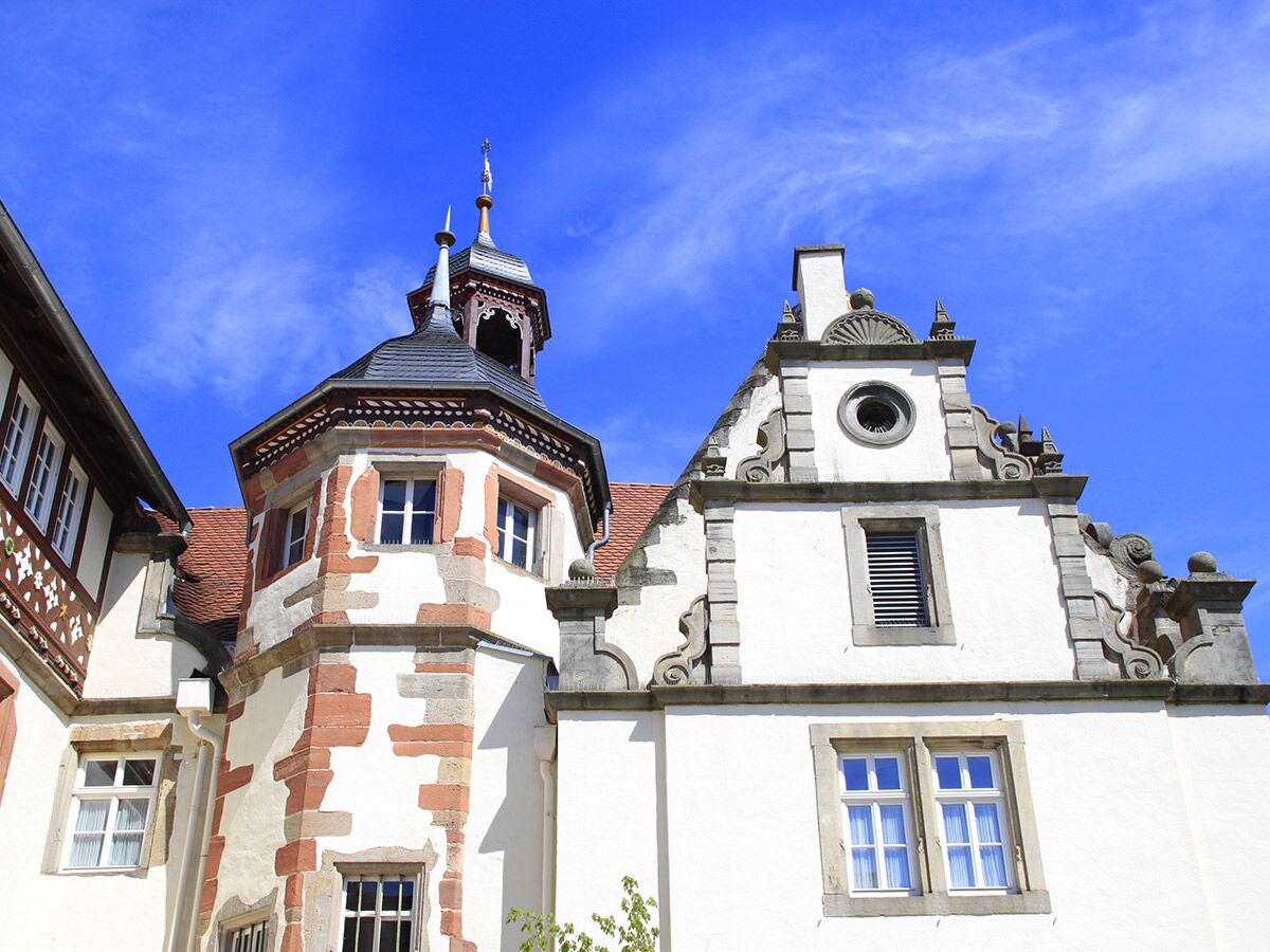 Nahaufnahme eines historischen Gebäudes mit einem oktogonalen Turm, dekorativen Giebeln und vielen Fenstern unter blauem Himmel.