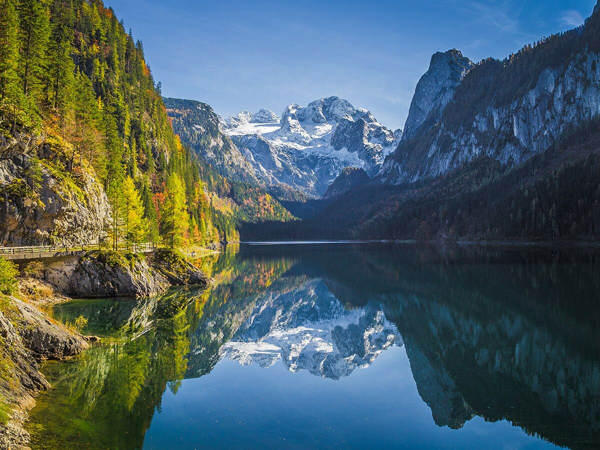 Malerischer Gosausee in den österreichischen Alpen im Herbst mit bunten Bäumen, schneebedeckten Bergen und deren Spiegelung im ruhigen Wasser.