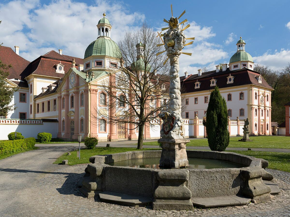 Barockes Kloster Fürstenfeld mit grünen Kuppeln, pink-gelber Fassade, und kunstvollem Brunnen im Innenhof.