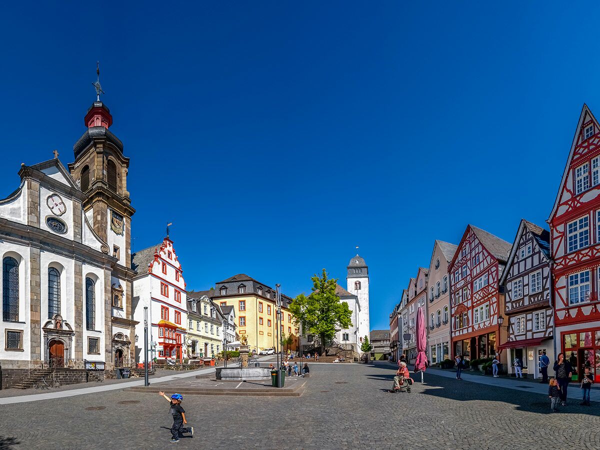 Marktplatz Attendorn mit Barockkirche, Fachwerkhäusern, Brunnen und spielenden Kindern unter blauem Himmel.