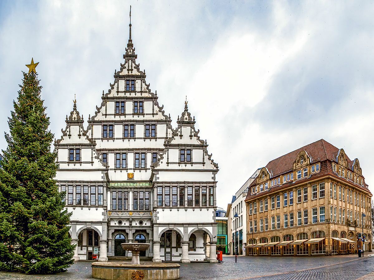 Historisches Rathaus Paderborn mit Weihnachtsbaum und Brunnen auf einem Marktplatz unter bewölktem Himmel.