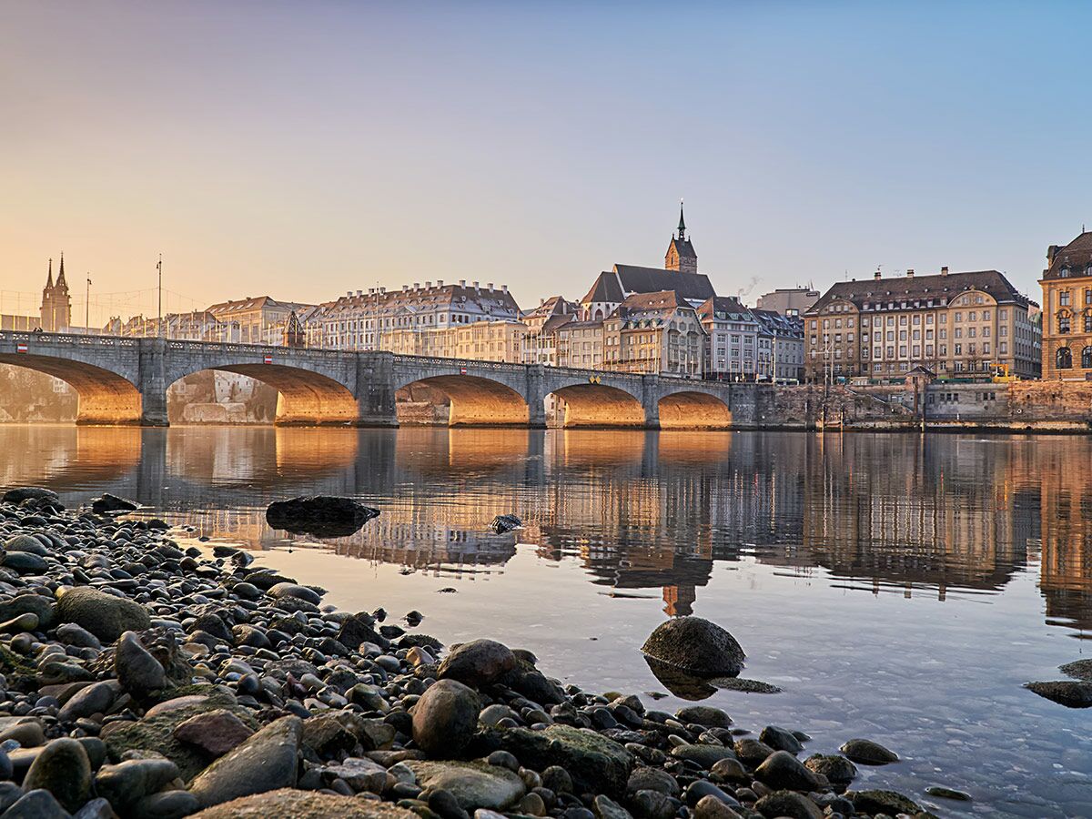 Historische Mittlere Brücke in Basel über den Rhein bei Sonnenaufgang mit Altstadt und Spiegelungen.