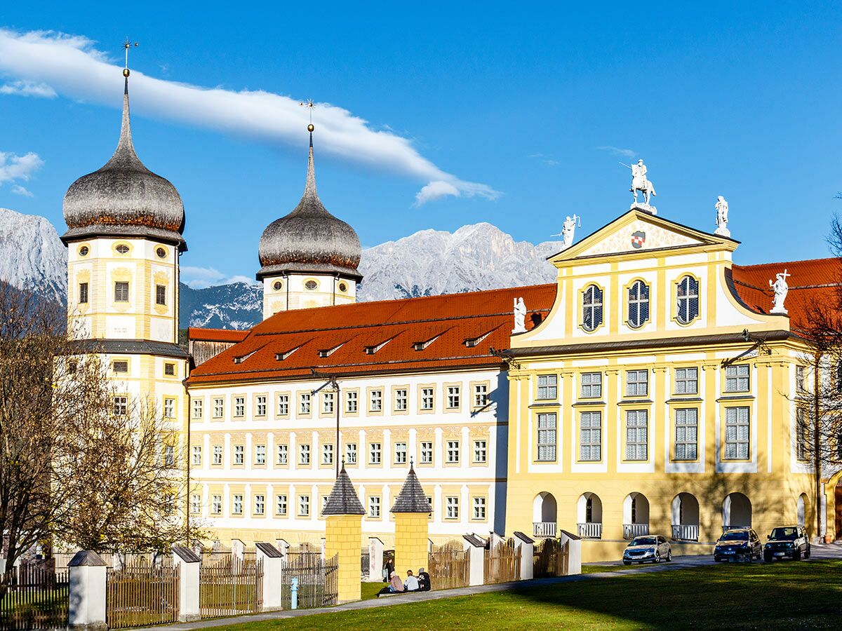 Kloster Ettal in Bayern mit Zwiebeltürmen und Barockfassade vor Alpenpanorama unter blauem Himmel.