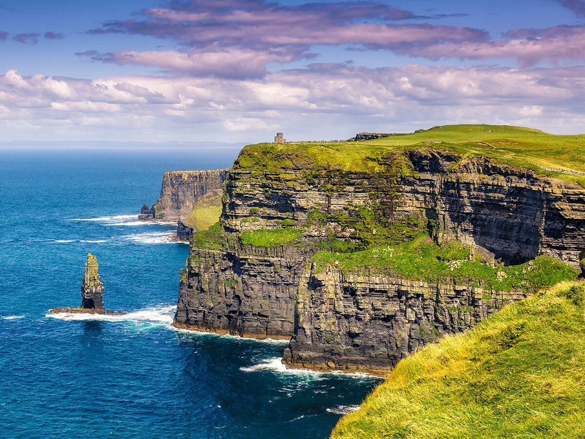 Majestätische Klippen von Moher, Irland, mit O'Brien's Tower und einer Felsnadel im blauen Atlantik unter Wolken.