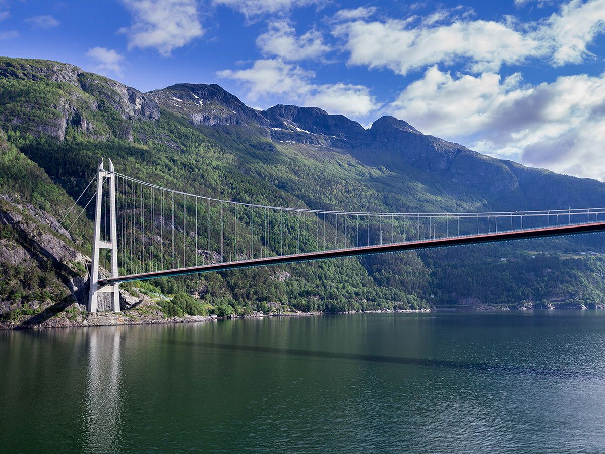 Eine majestätische Hängebrücke überspannt einen norwegischen Fjord, umgeben von grünen Bergen und klarem Himmel.