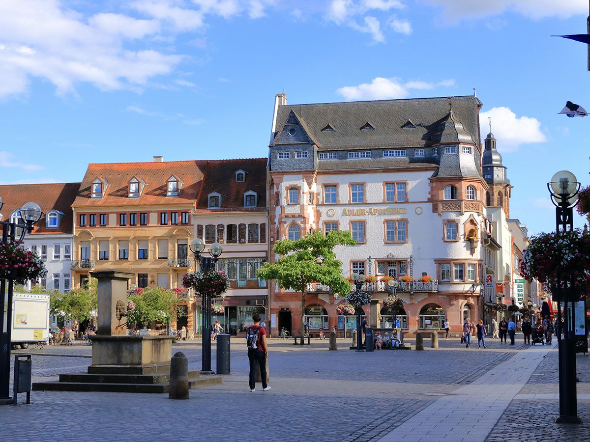 Blick auf einen sonnigen historischen Marktplatz in Deutschland mit der Adler-Apotheke, traditionellen Gebäuden und Menschen.