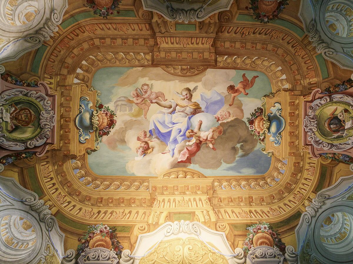 Opulentes Deckenfresko im Barockstil mit schwebender allegorischer Figur und Putten auf Wolken, umgeben von Goldornamenten.