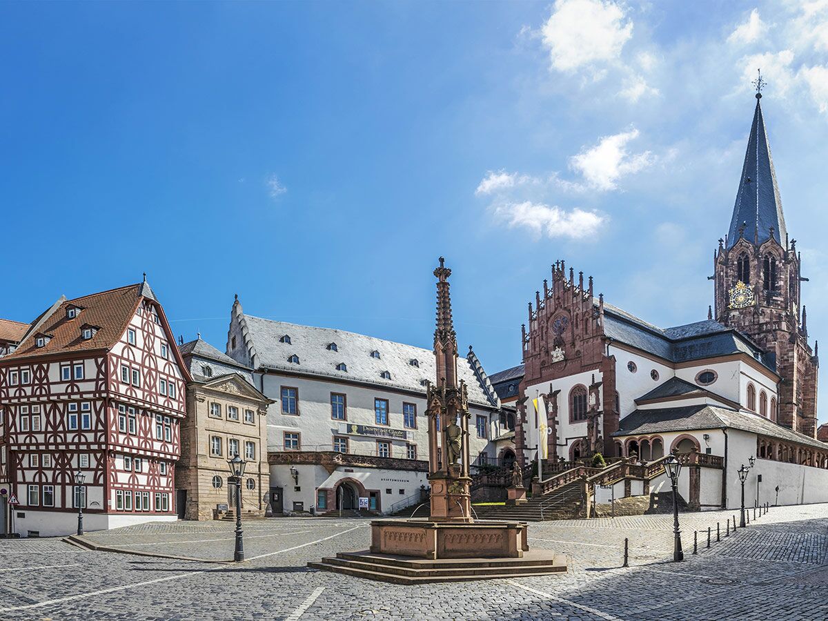 Malerischer Marktplatz mit historischem Brunnen, Fachwerkhäusern und imposanter Stiftskirche unter blauem Himmel.