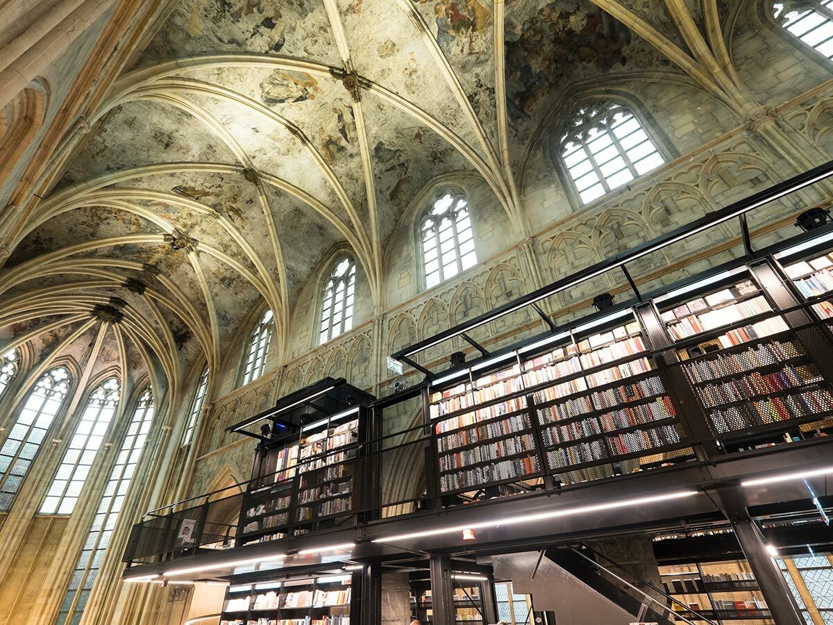 Moderne Bibliothek in historischer Kirche mit hohen Gewölbedecken, gotischen Fenstern und mehrstöckigen Bücherregalen.