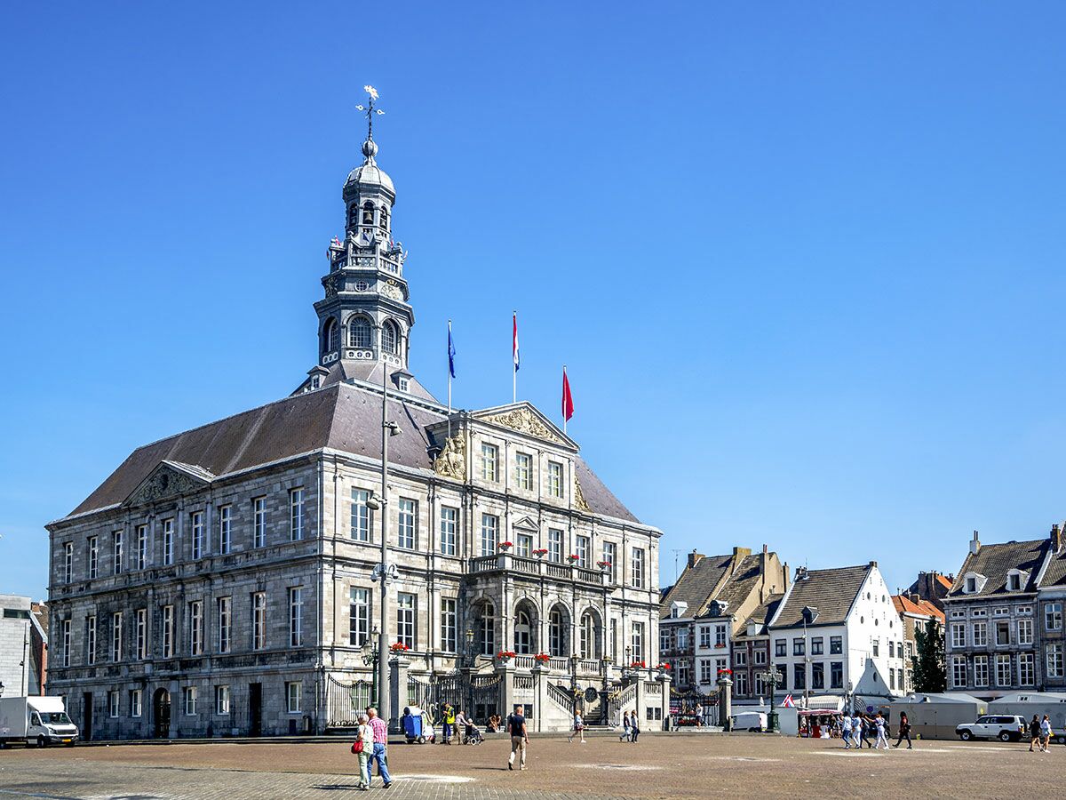 Historisches Rathaus in Maastricht mit Turm, Glockenspiel, Treppen und Menschen auf sonnigem Marktplatz.