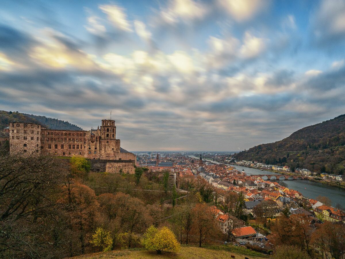 Panorama von Heidelberg mit Schloss, Altstadt, Neckar und Herbstwäldern unter bewölktem Himmel mit Langzeitbelichtung.