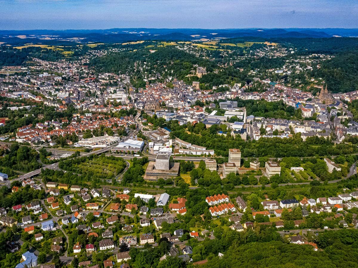 Luftaufnahme von Siegen, Deutschland, mit dicht bebauten Stadtvierteln, Wäldern, Hügeln und Autobahn im Sommer.