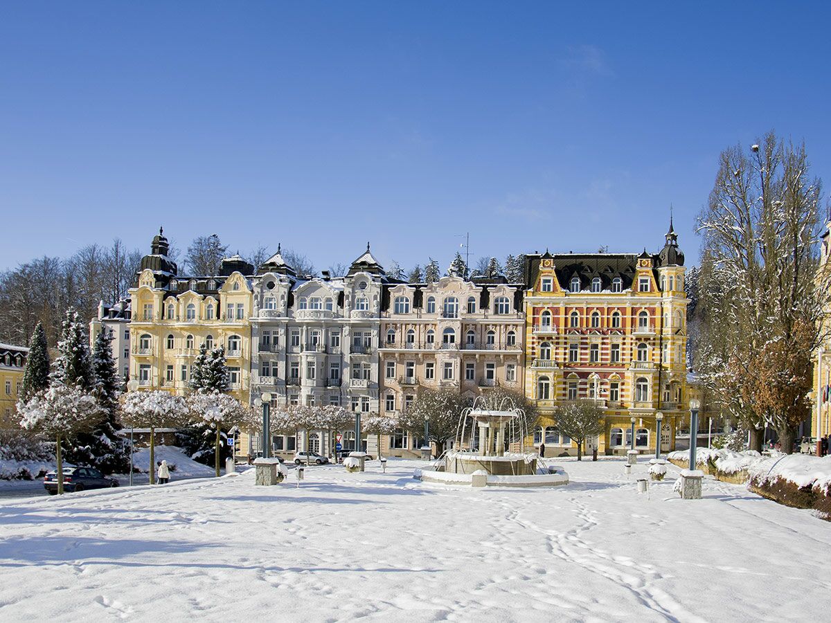 Historische Jugendstilgebäude in Karlovy Vary, Tschechien, verschneit an einem sonnigen Wintertag mit Brunnen.