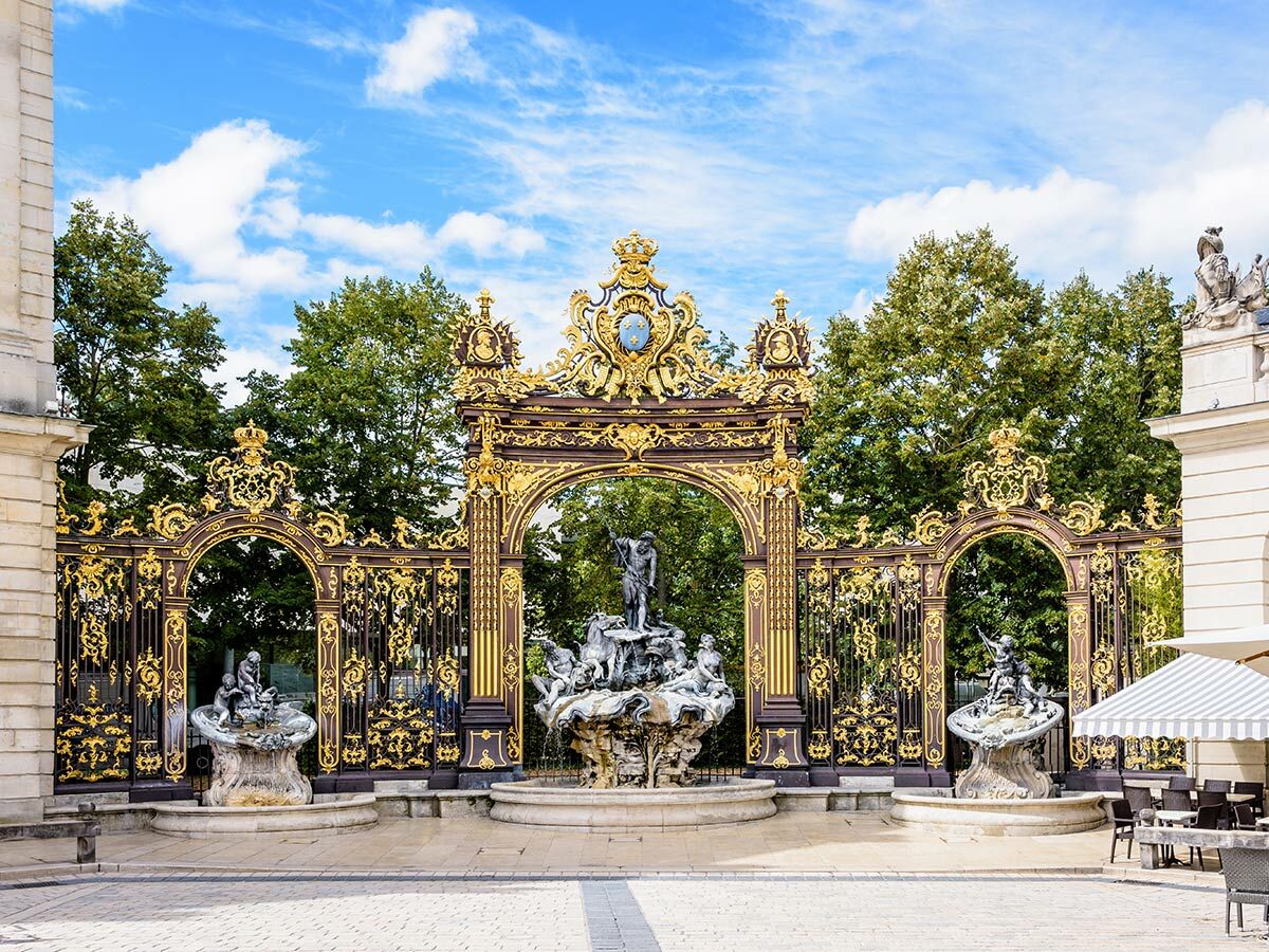 UNESCO-Weltkulturerbe Place Stanislas in Nancy, Frankreich, mit opulenten goldenen Toren und Brunnen unter blauem Himmel.