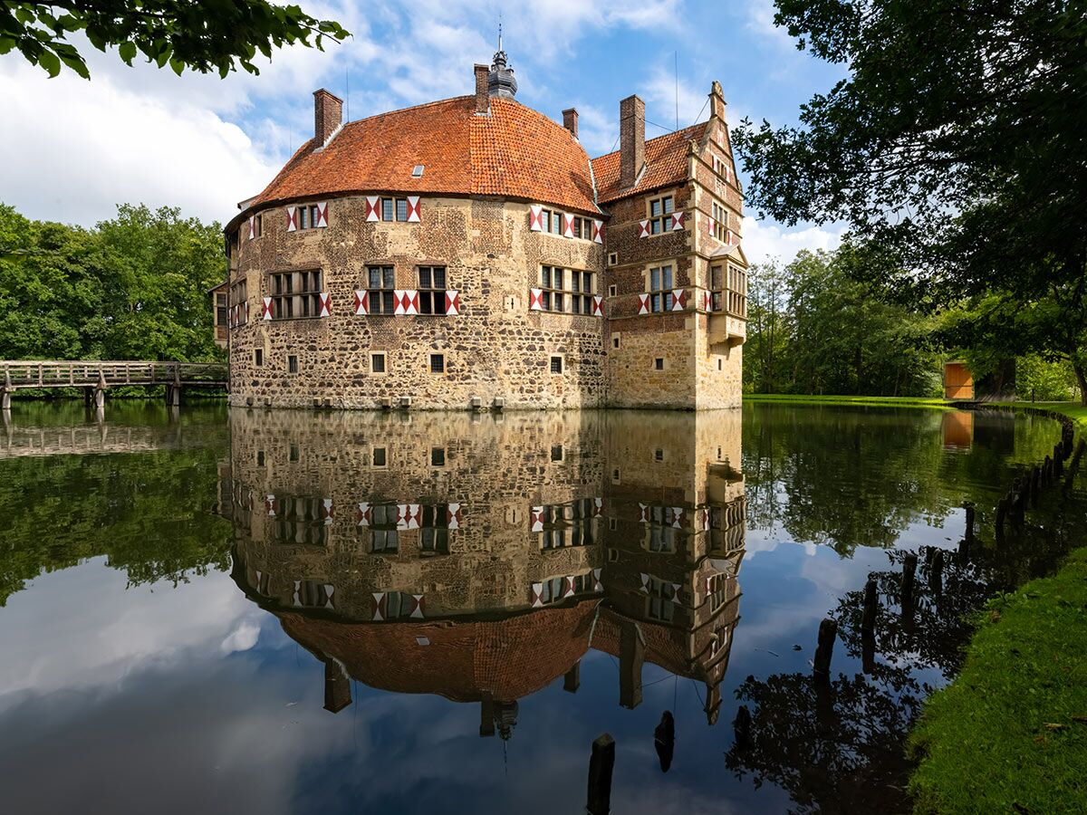 Historisches Wasserschloss Vischering in Lüdinghausen, Deutschland, spiegelt sich im ruhigen Wasser, umgeben von Bäumen.