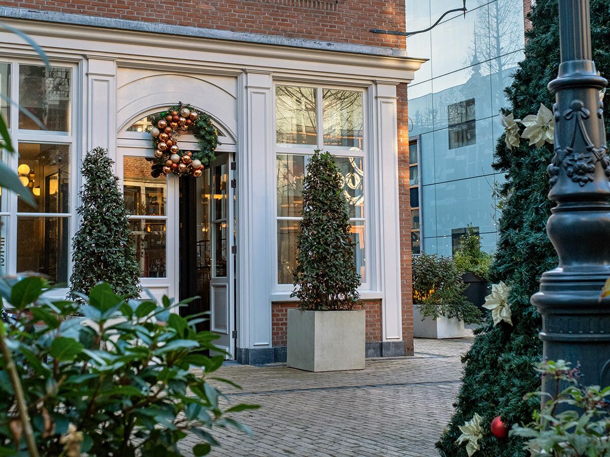 Festlich geschmückte Hausfassade mit Weihnachtsbaum, Kranz und goldenen Kugeln in urbaner Winterlandschaft.