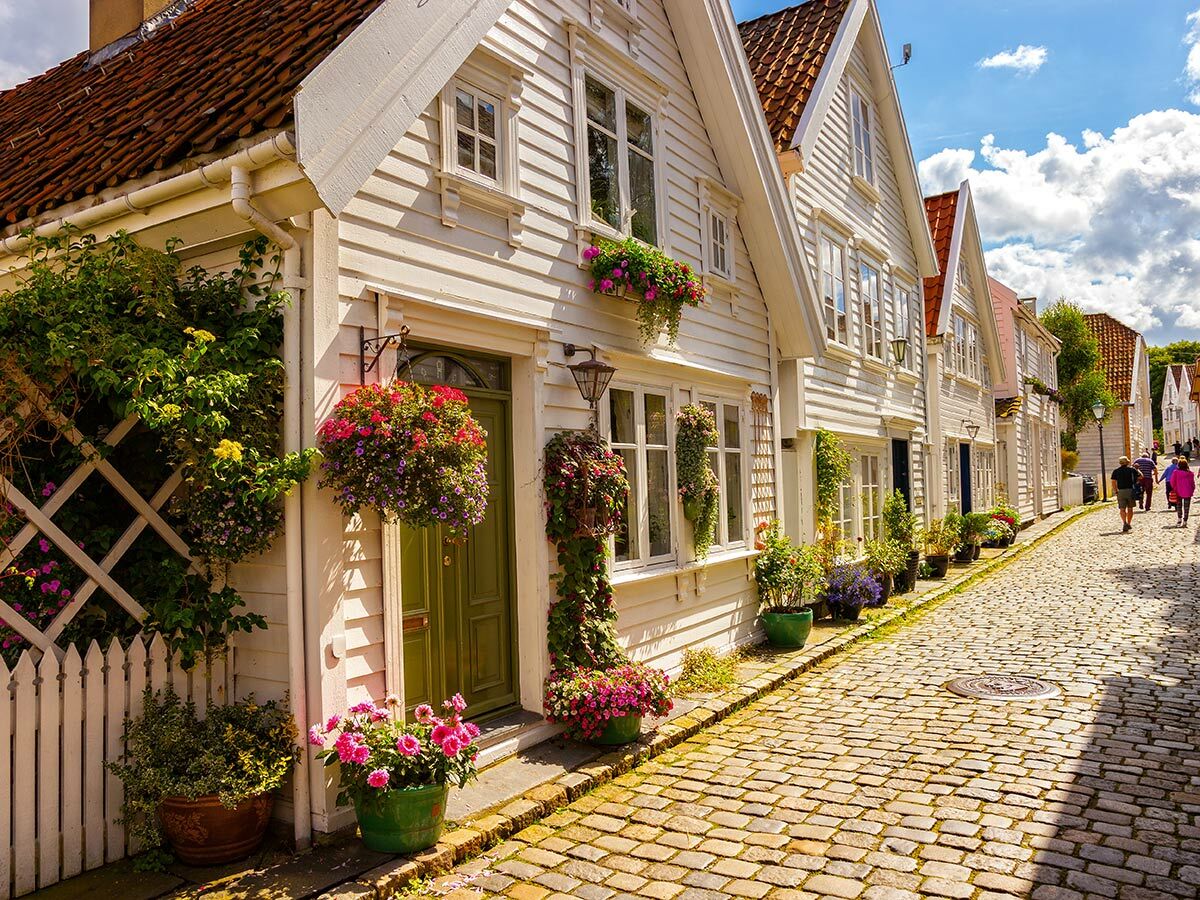 Malerische Gasse in Gamle Stavanger, Norwegen, mit weißen Holzhäusern, roten Dächern, Kopfsteinpflaster und bunten Blumen.