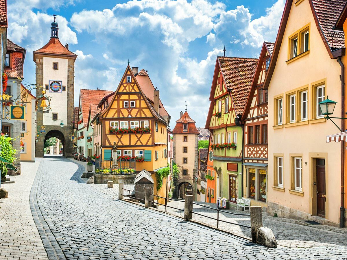 Malerische Kopfsteinpflastergasse im historischen Rothenburg ob der Tauber mit Fachwerkhäusern, Stadttor und blauem Himmel.