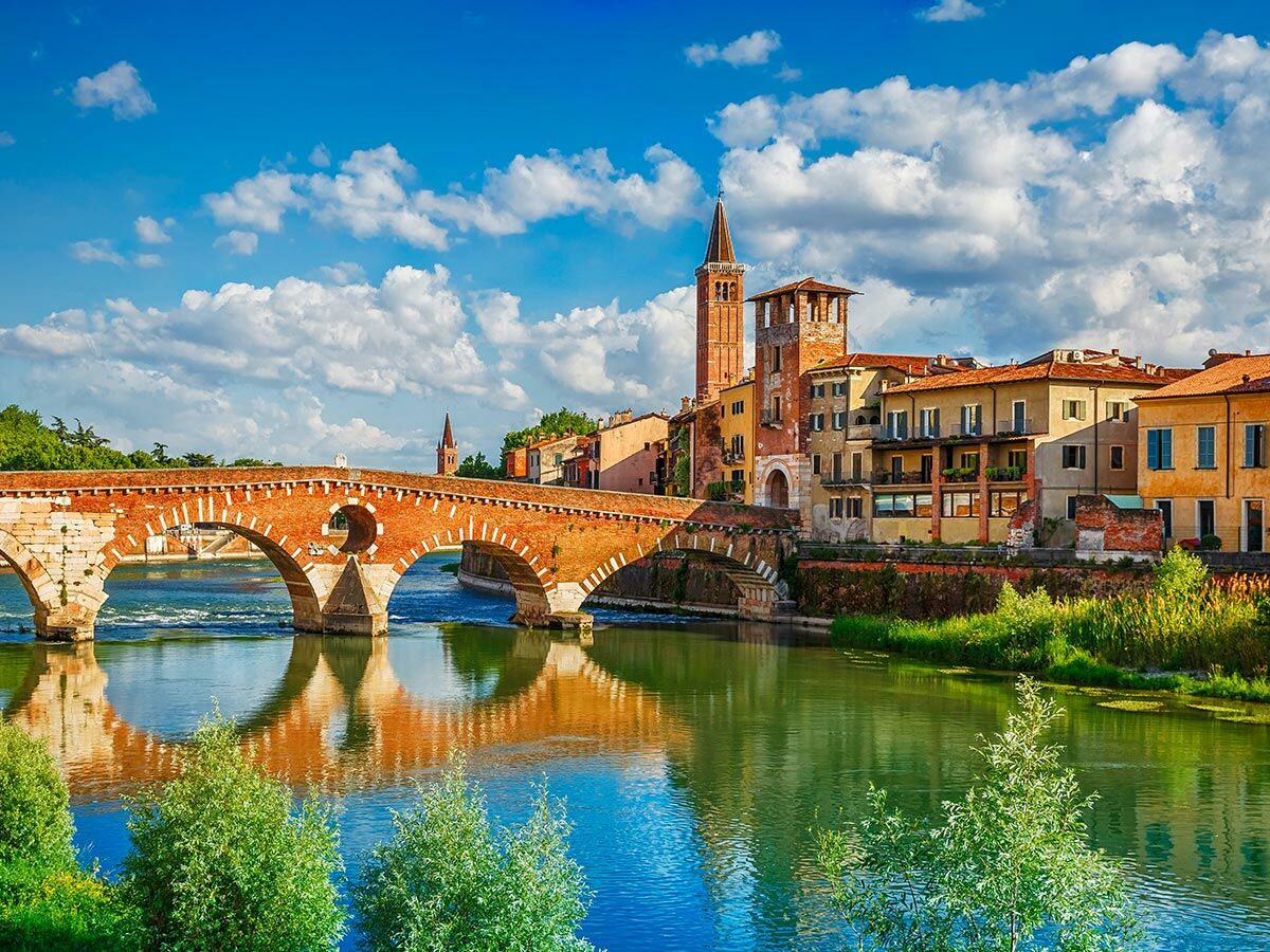 Historische Ponte Pietra Brücke über den Fluss Adige in Verona, Italien, mit Altstadt, Kirchturm und blauem Himmel.