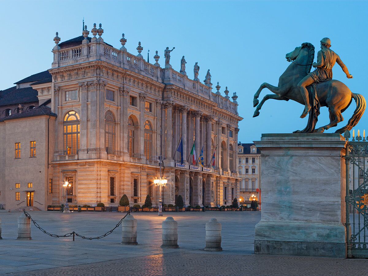 Palazzo Madama in Turin mit Reiterstatue auf der Piazza Castello bei Abenddämmerung, beleuchtete Fassade.
