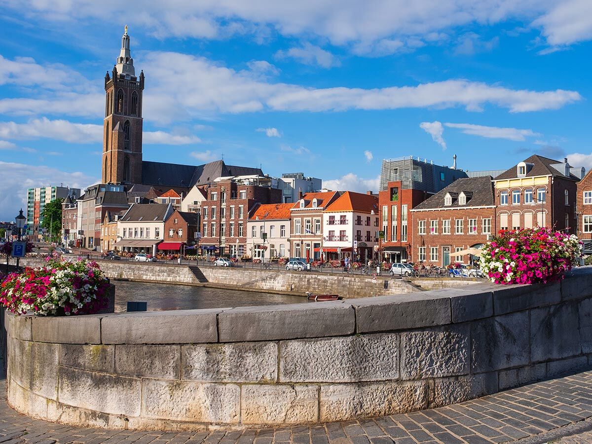 Blick auf die historische Stadt Roermond in den Niederlanden mit der Munsterkerk, bunten Gebäuden und einem Kanal mit Blumen am Ufer.