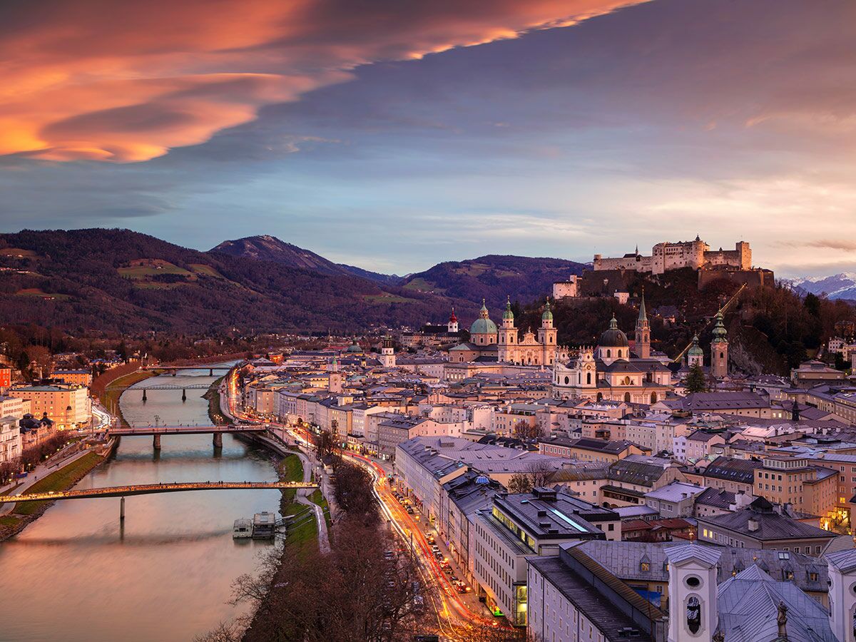Panoramablick auf Salzburg bei Dämmerung mit erleuchteter Festung Hohensalzburg, Salzach Fluss, Brücken und Bergen.