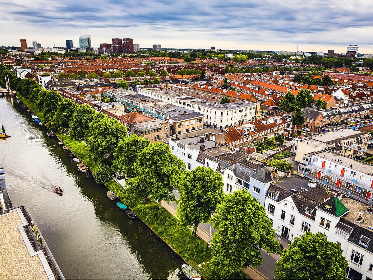 Luftaufnahme einer europäischen Stadt mit Kanal, grünen Bäumen, vielen Häusern und einem Motorboot auf dem Wasser.