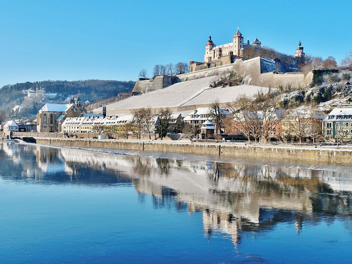 Würzburgs Marienberg Festung und Altstadt am Main im Winter mit Schnee und Spiegelung im Fluss.