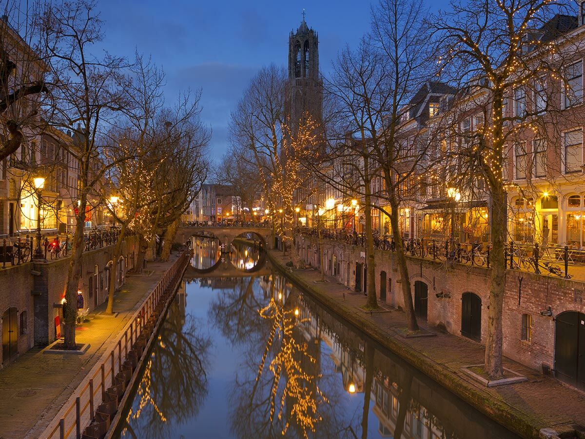 Stimmungsvoller Oudegracht Kanal in Utrecht bei Nacht mit beleuchteten Bäumen, Brücken und Domturm, Spiegelungen im Wasser.