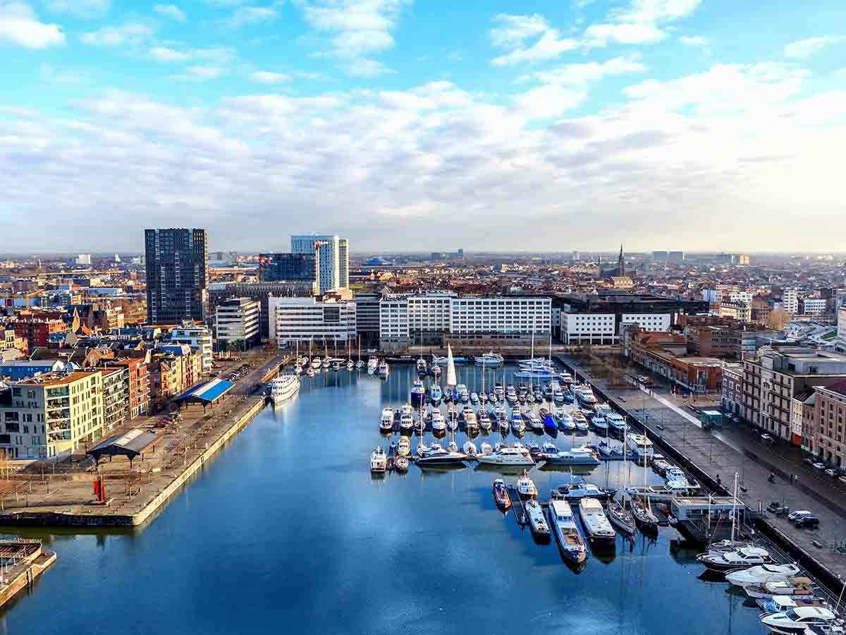 Luftaufnahme des Antwerpener Hafens mit Yachthafen, Gebäuden, Stadtsilhouette und blauem Himmel.