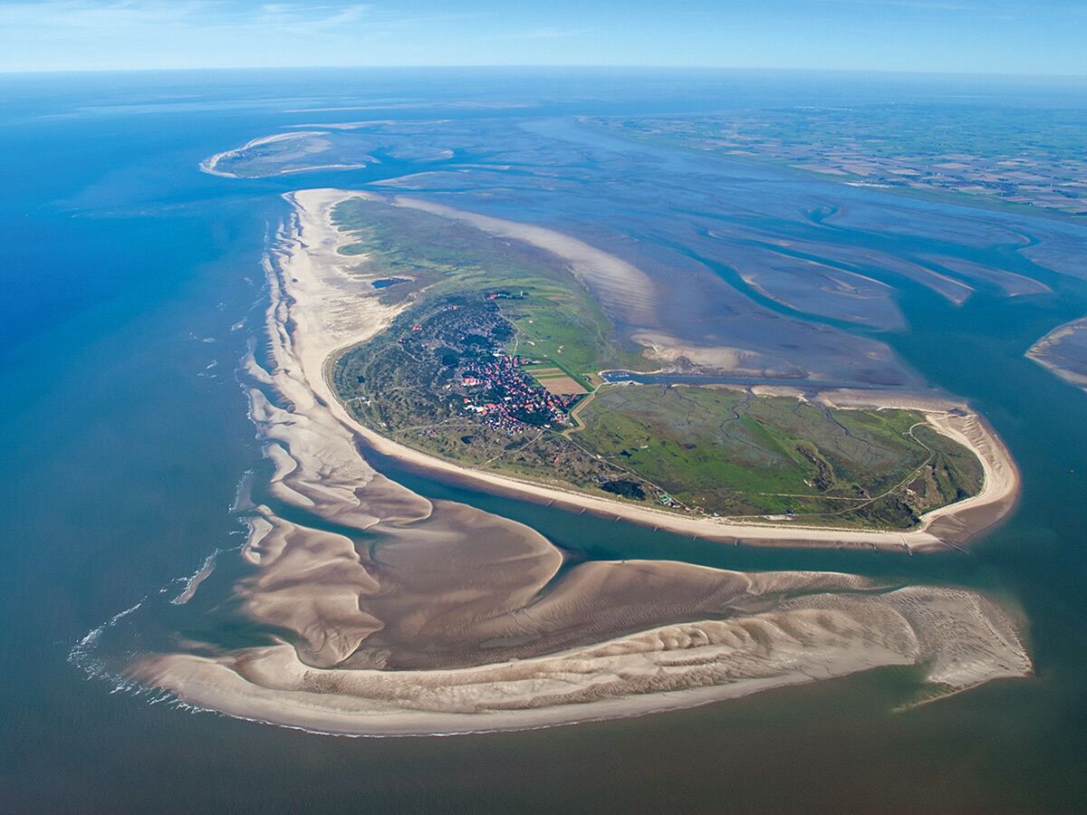 Luftaufnahme einer Nordseeinsel mit Stadt, Dünen, Stränden und weiten Sandbänken im Wattenmeer bei klarem Himmel.