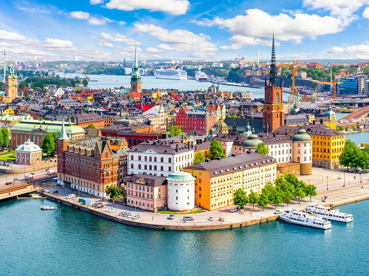 Luftaufnahme von Stockholms historischer Altstadt Gamla Stan mit bunten Gebäuden, Kirchen und Schiffen am blauen Wasser.